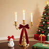 Gold candlestick holder with a red velvet bow and white candle next to a small snowman decoration.