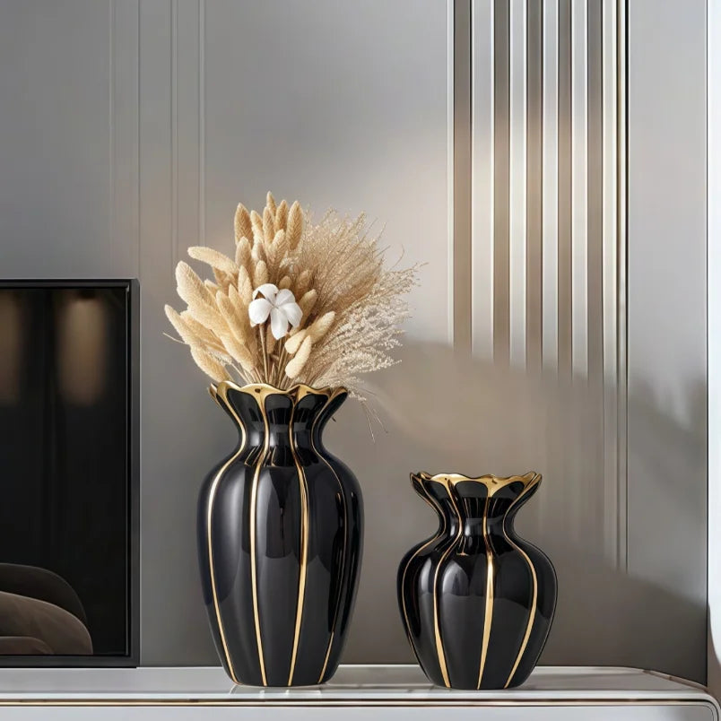 A black ceramic flower vase with gold accents sits on a shelf next to a vertical decorative panel.