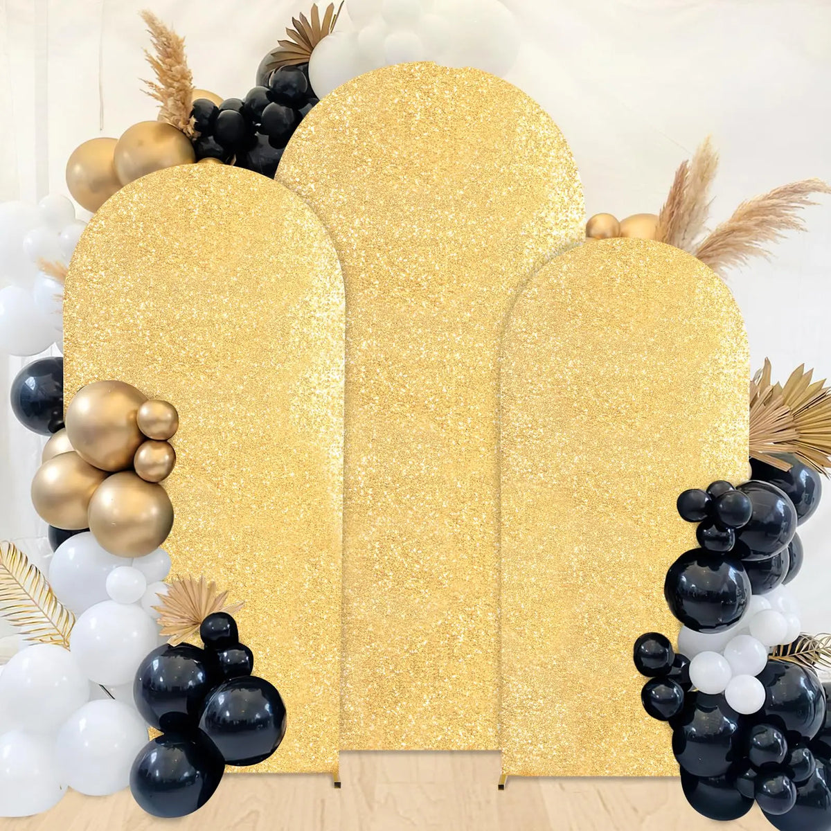 A golden sequin arch backdrop decorated with black and white spherical elements and dried grasses.