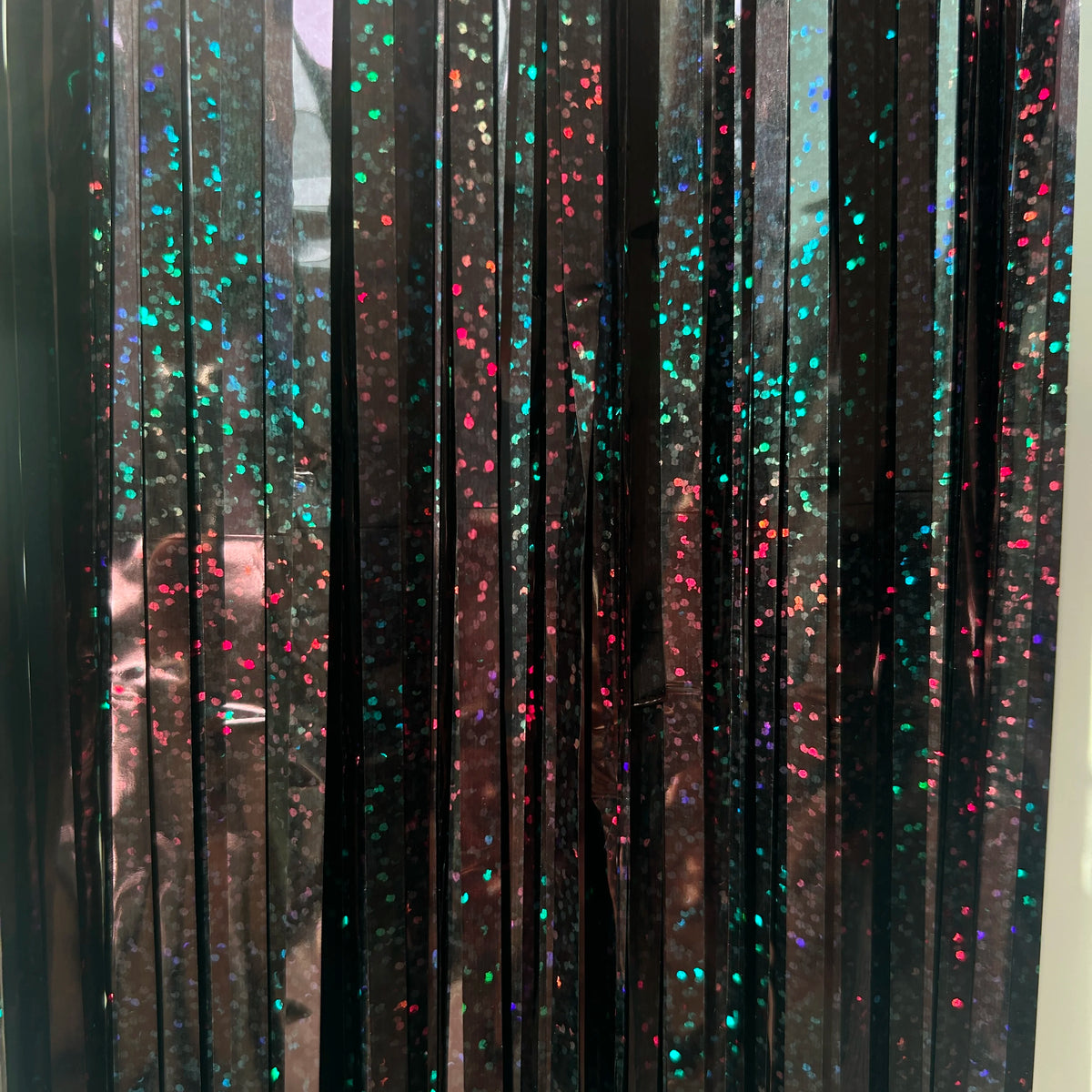 A vertical display of metallic tinsel foil fringe curtain backdrop featuring iridescent pink and blue glitter accents.