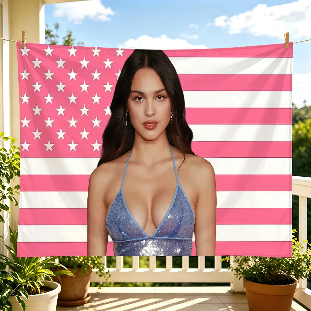 A woman wearing a blue sparkly top stands in front of a pink and white striped flag tapestry.