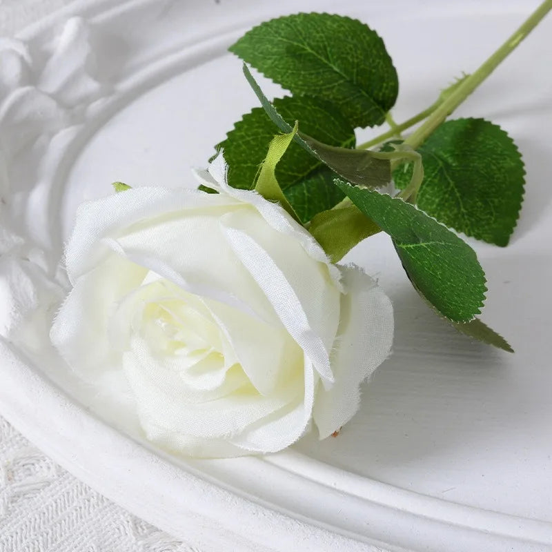 White velvet artificial rose with green leaves on a white plate