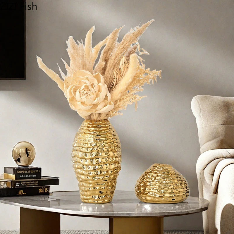 A golden wrinkle ceramic tabletop vase with dried floral arrangements sits on a marble table.