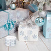 White and blue gift boxes decorated with snowflake patterns and wrapped in festive silver ribbon, surrounded by pine branches