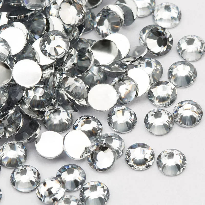 A close-up view of many clear, round flatback resin rhinestones scattered on a white background.