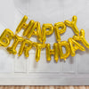 A golden foil letter balloon banner spelling out Happy Birthday hanging on a white wall.