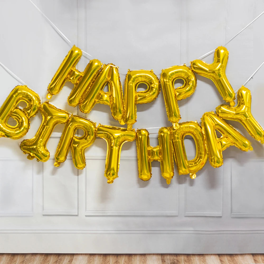 A golden foil letter balloon banner spelling out Happy Birthday hanging on a white wall.