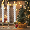 Three white taper candles in a set are displayed next to a decorated Christmas tree and bokeh lights.