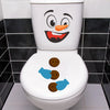A white toilet featuring a funny cartoon face decal with large eyes and an orange nose, set against a black and white tiled b