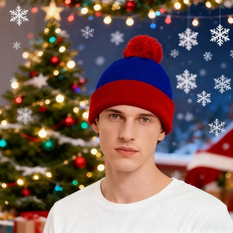A young man wearing a red knitted beanie with a fluffy pompom and a white shirt, standing in front of a decorated Christmas t