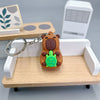 Pendentif de capybara orange avec accessoire vert sur une étagère en bois à côté d'un appareil électronique blanc.