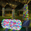 A long, cylindrical rope light with multicolored LED strands illuminates a grassy outdoor area near decorated trees.