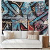 A modern living room featuring a white sofa adorned with neutral pillows and a large urban graffiti tapestry hanging on the w