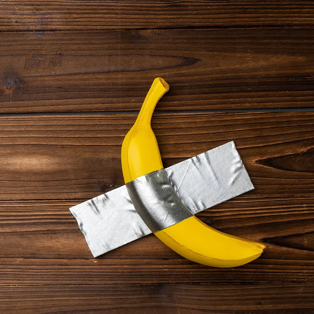 A yellow banana sculpture is crossed with a silver ribbon on a dark wooden surface.