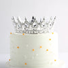 Gâteau à étages blanc décoré d'accents dorés et surmonté d'une couronne élégante en cristal et métal.