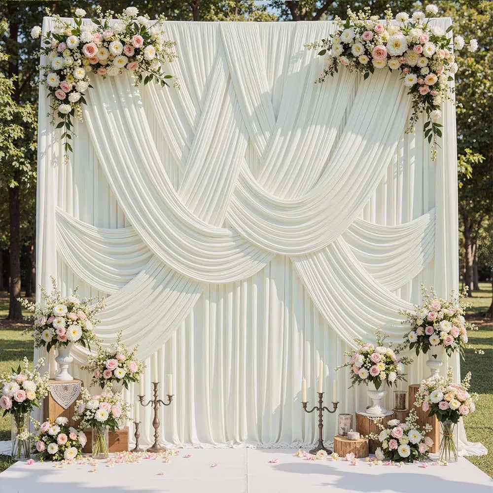 A white satin backdrop curtain with vertical pleats and draped folds decorated with floral arrangements for photography.