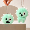 A bright green fuzzy plush keychain with a face design is hanging from a silver chain.