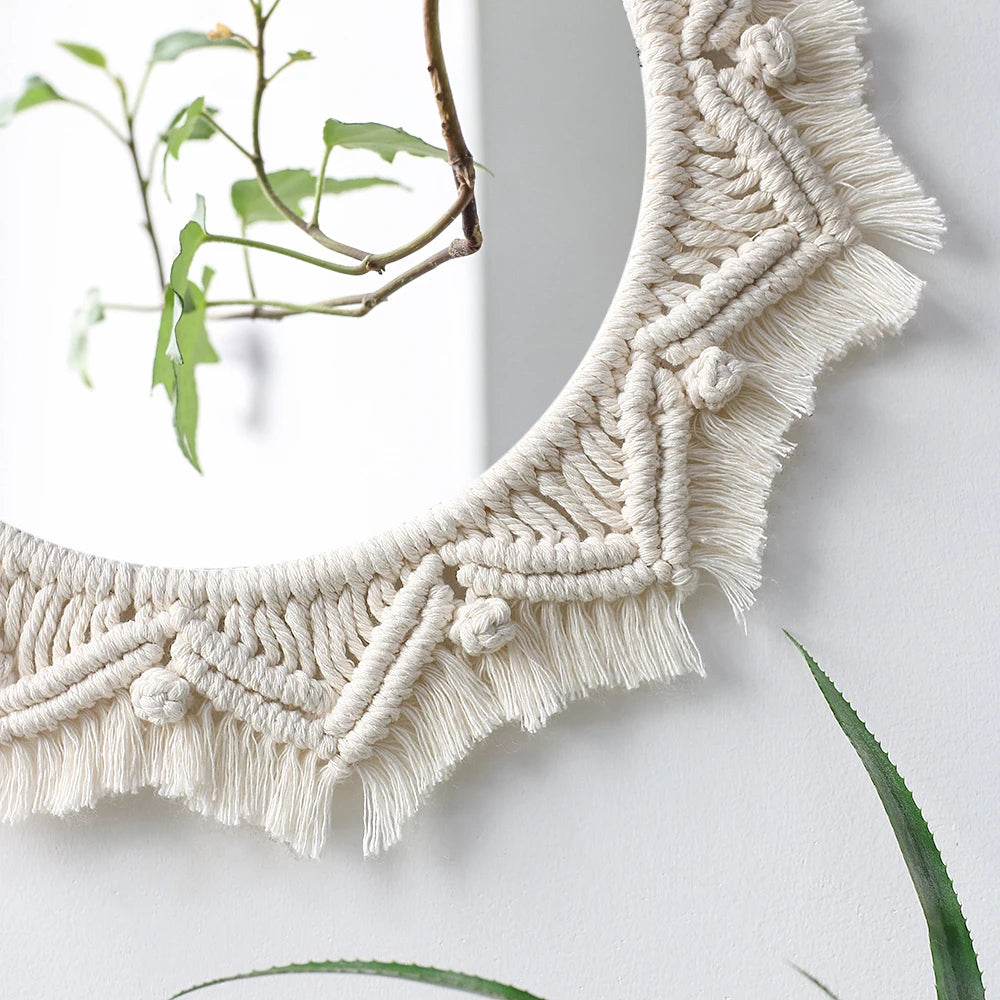 A round macrame wall mirror with a textured, cream-colored fringe hanging on a white wall.