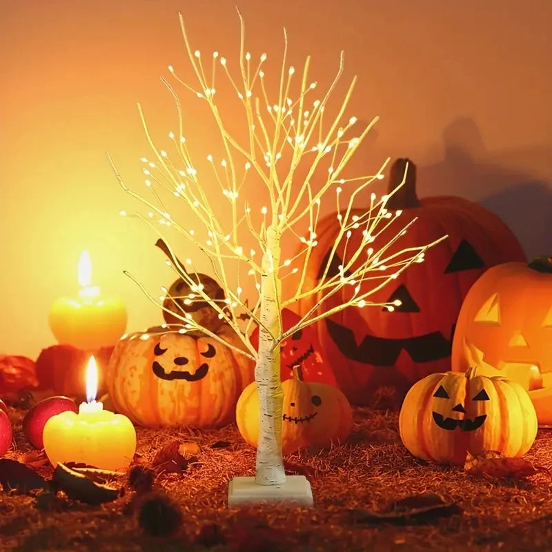 An LED birch tree decorative light illuminated in a Halloween-themed setting with pumpkins and glowing candles.