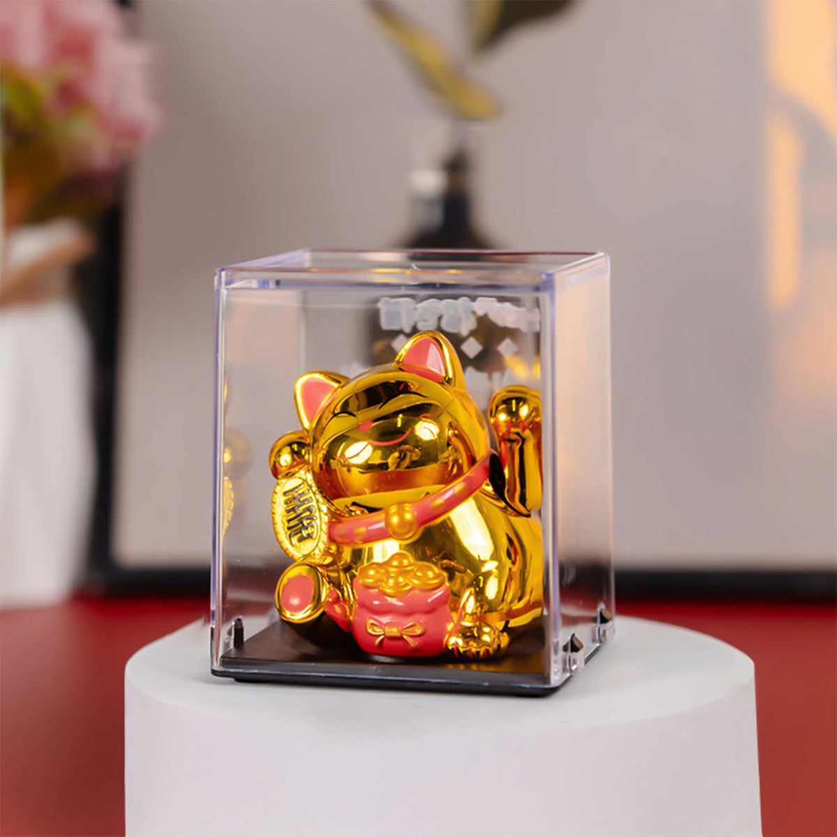 A golden solar-powered waving lucky cat figurine displayed in a clear acrylic box.