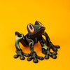 A dark green tree frog ornament with large orange eyes is displayed against a bright orange background.