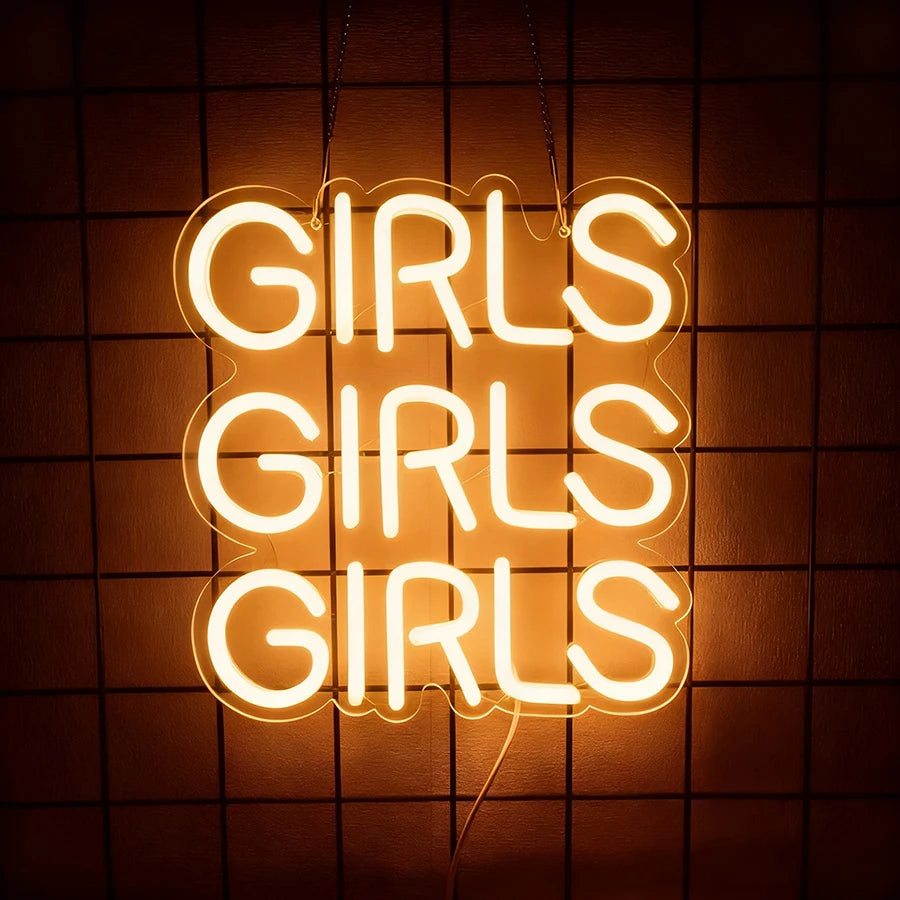 A glowing neon sign spelling out GIRLS in a rounded font against a dark, grid-patterned background.