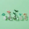 A collection of decorative glass vials and vessels holding dried pink and blue floral sprigs on a light green background.