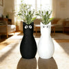 A pair of cat-shaped vases, one black and one white, standing on a light rug.