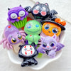 A collection of colorful Halloween resin charms featuring purple owls, black bats, green monsters, and purple spiders on a wh