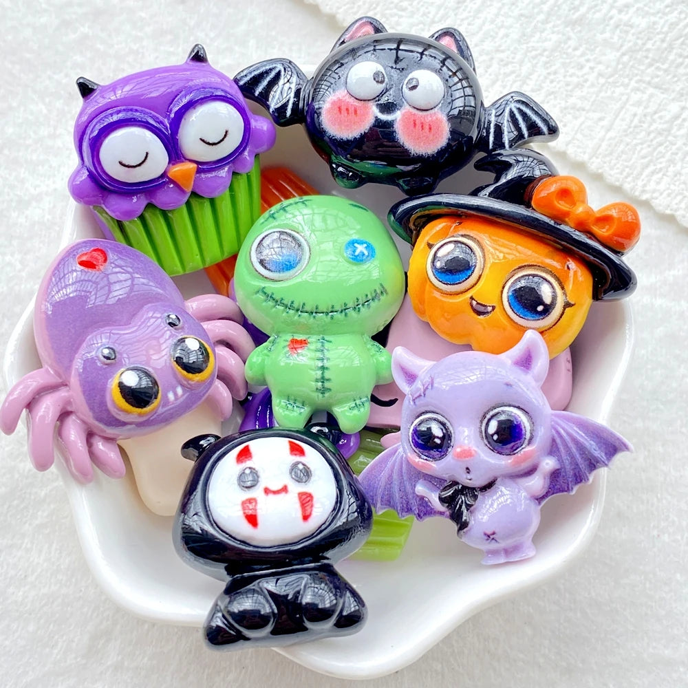 A collection of colorful Halloween resin charms featuring purple owls, black bats, green monsters, and purple spiders on a wh