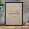A framed canvas print featuring the quote Progress, not perfection, in green text on a beige background.