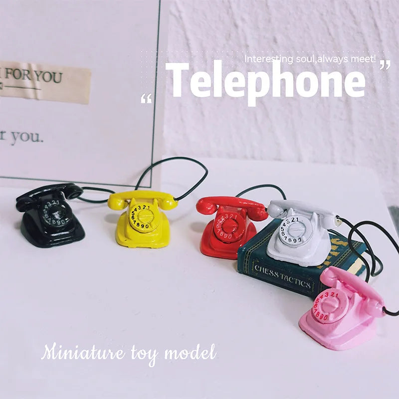 A collection of miniature vintage rotary desk telephones in black, yellow, red, and white on a white surface.