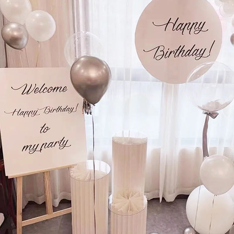 Une décoration avec des ballons et un panneau de bienvenue pour une fête, sur un fond de rideau blanc transparent.