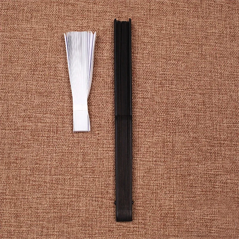 Un éventail main squelette en bambou pliante noir posé sur un fond de tissu tissé marron.