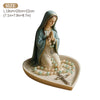 A statue of the Virgin Mary with a hood and a rosary holder on a tray