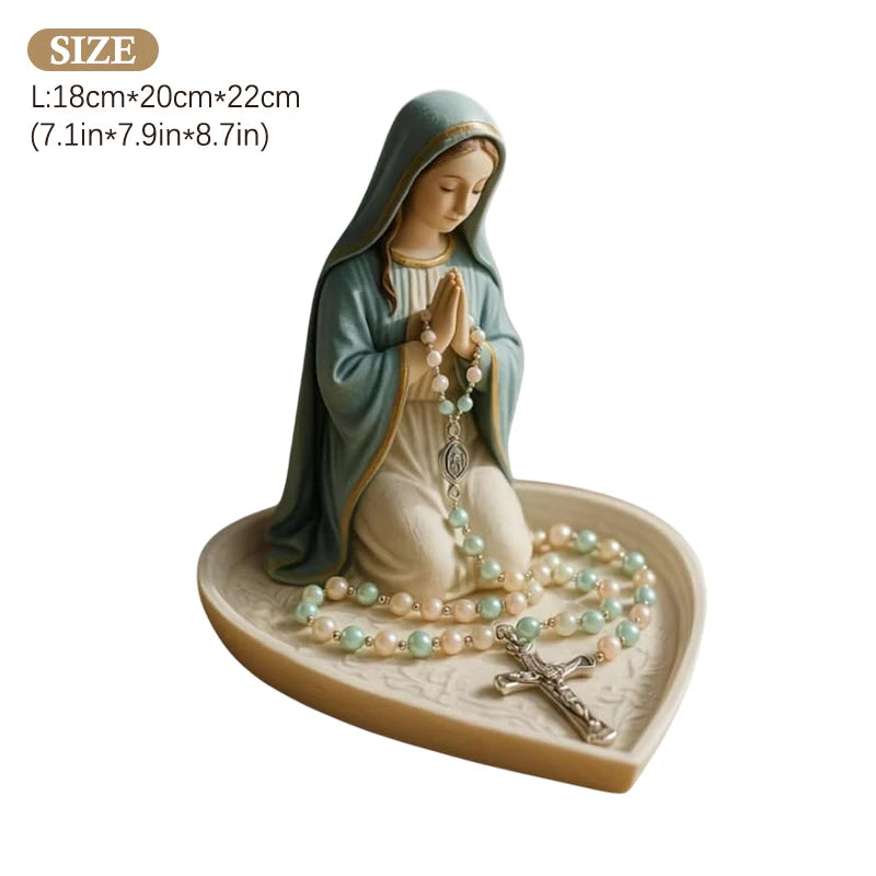 A statue of the Virgin Mary with a hood and a rosary holder on a tray