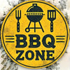 Panneau rond jaune avec texte noir indiquant BBQ ZONE, entouré de feuilles décoratives blanches.