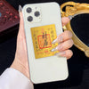 A hand holds a smartphone featuring a gold wealth amulet sticker against a dark background with a gold-framed mirror.
