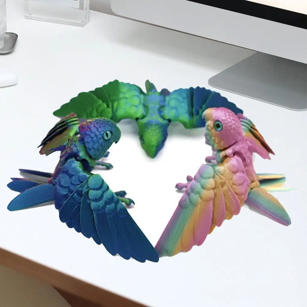 A set of three articulated 3D printed parrot figurines with movable wings in shades of green, blue, and pink.