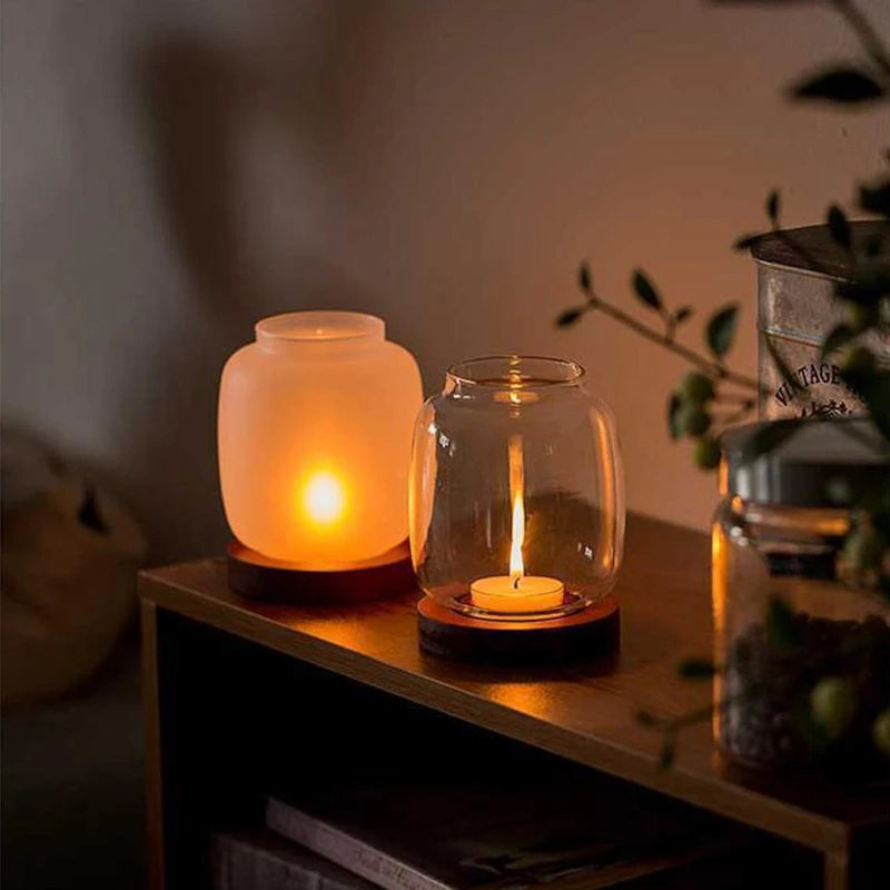 A vintage wooden candle lantern with a glass cover holding a lit candle on a dark wooden surface.