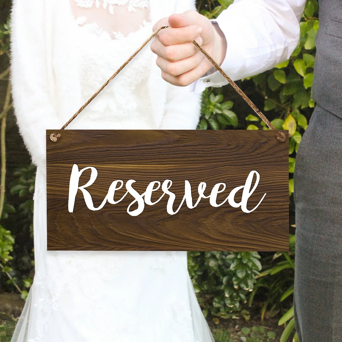 A person holds a rustic wooden sign with the word Reserved written on it, set against a green outdoor background.