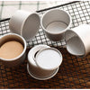 A set of five white non-stick round cake molds with removable bases arranged on a black wire mesh grid.
