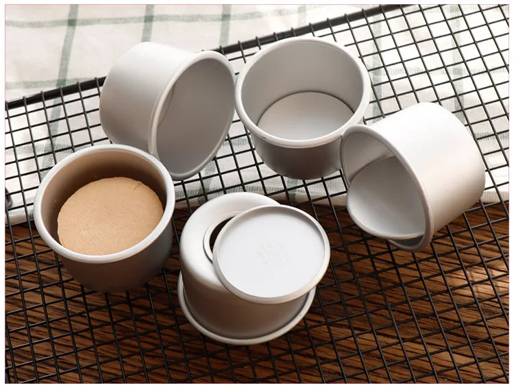 A set of five white non-stick round cake molds with removable bases arranged on a black wire mesh grid.