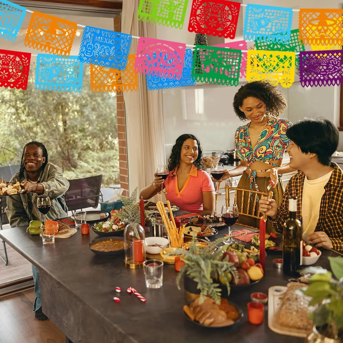 A group of people celebrating with a colorful papel picado bunting banner strung across the background.