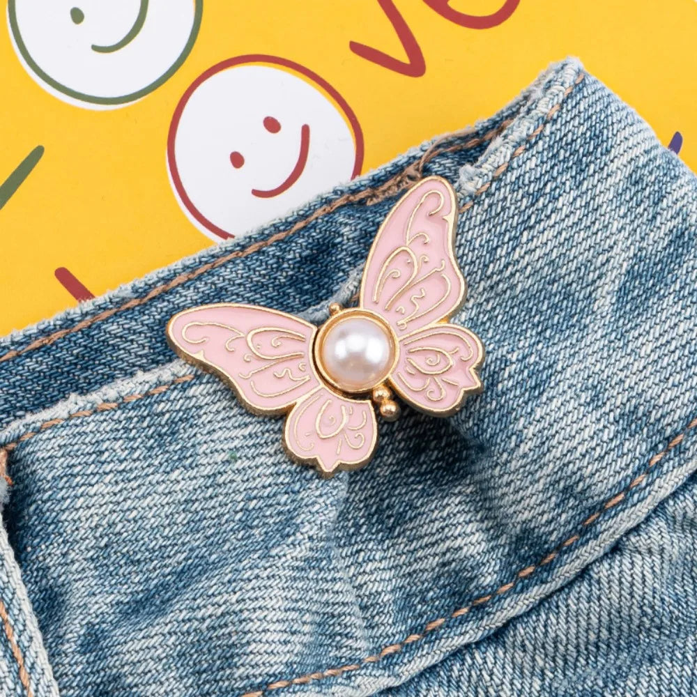 A pink butterfly clip with a pearl accent is attached to a denim jean pocket.