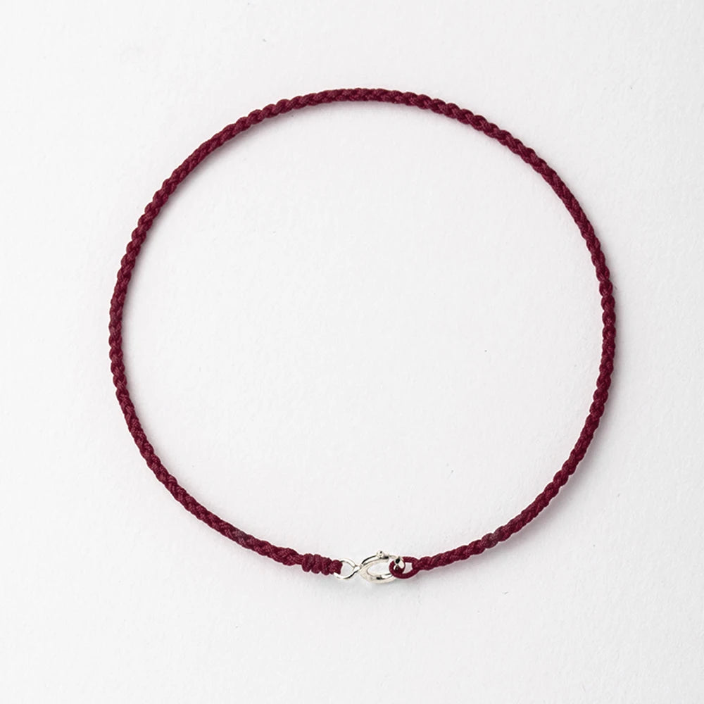A handmade red string bracelet with a gold plated clasp laid flat against a white background.