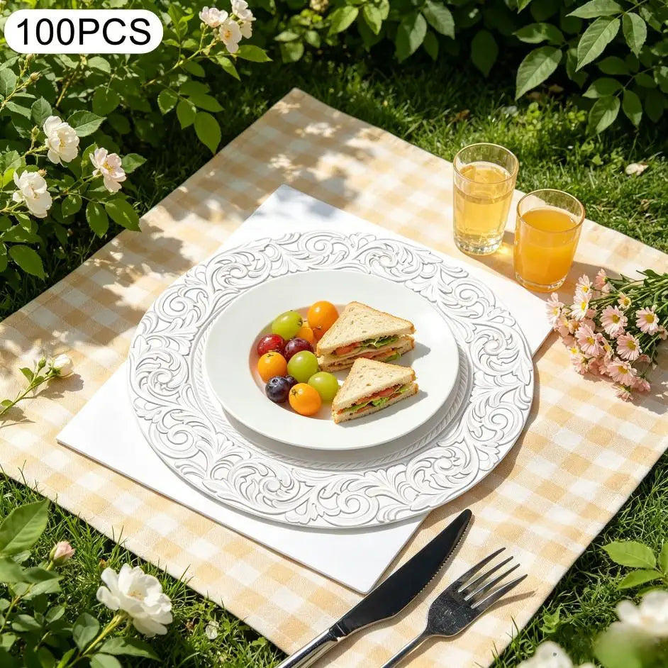 A set of silver embossed charger plates is displayed on a checkered mat with fruit and cutlery in a garden setting.