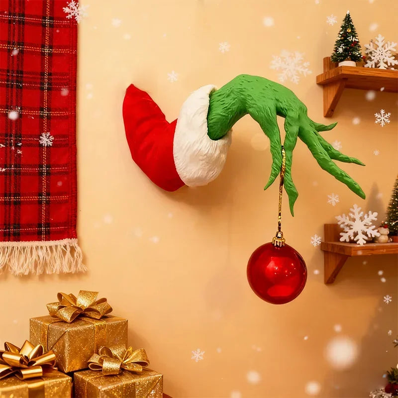 A green monster arm decoration with a red nose hangs on a wall next to wrapped gifts.