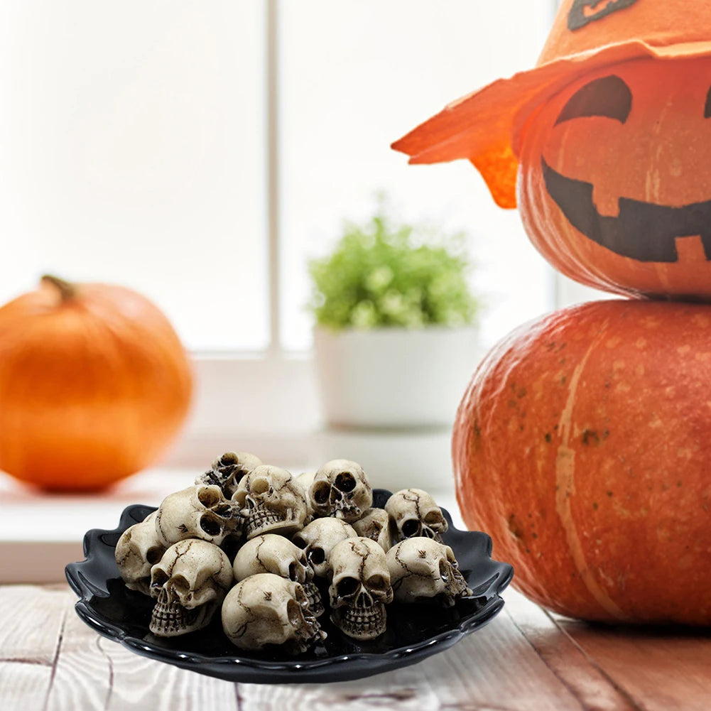 A set of realistic skull figurines displayed in a black dish next to pumpkins.