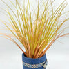 A bundle of artificial grass greenery with golden and reddish-brown blades planted in a blue pot.